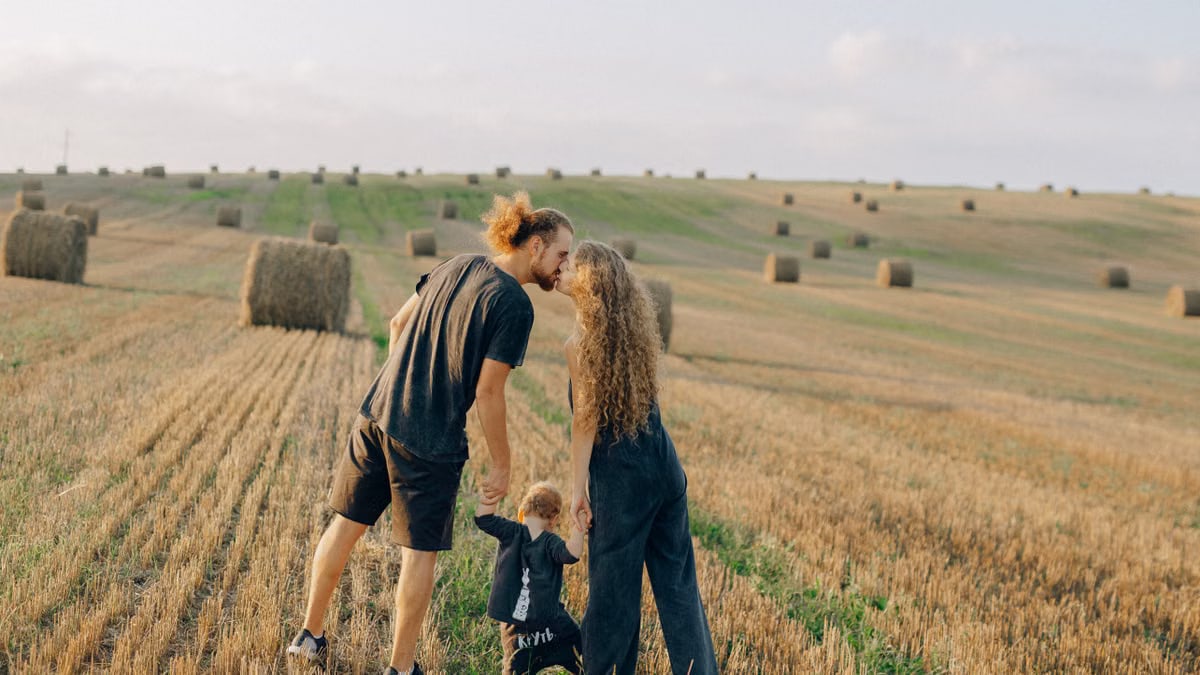 A couple with their child enjoy a sunny day in a wheat field, symbolizing love and joy.